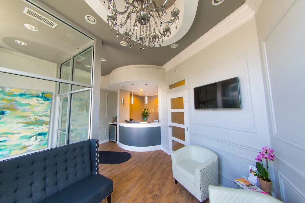 A bright reception area featuring a classic crystal chandelier, a blue tufted sofa, and a clean white front desk