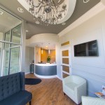 A bright reception area featuring a classic crystal chandelier, a blue tufted sofa, and a clean white front desk