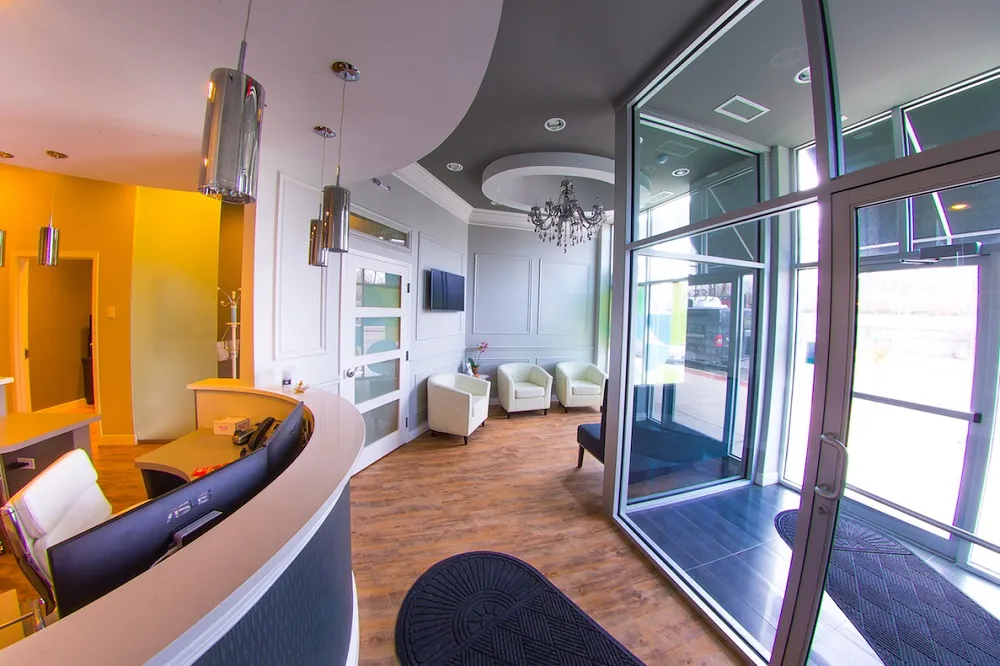 Wide-angle shot of a modern dental office entrance with warm yellow walls, curved wood paneling, and a large glass door