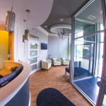 Wide-angle shot of a modern dental office entrance with warm yellow walls, curved wood paneling, and a large glass door