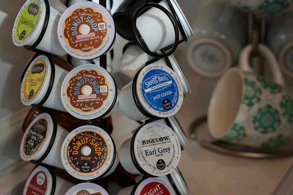 A close-up of various coffee pods (K-Cups) and a decorative ceramic mug, highlighting the office's refreshment amenities