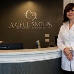 A female dentist in a white lab coat standing confidently next to the curved reception desk in the clinic lobby.