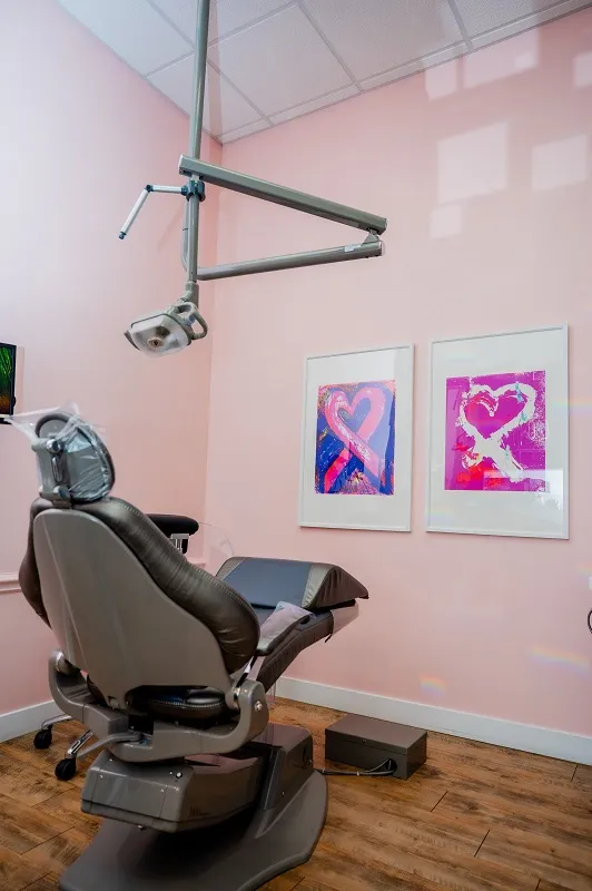 A dental treatment room with soft pink walls, a comfortable patient chair, and colorful abstract art pieces