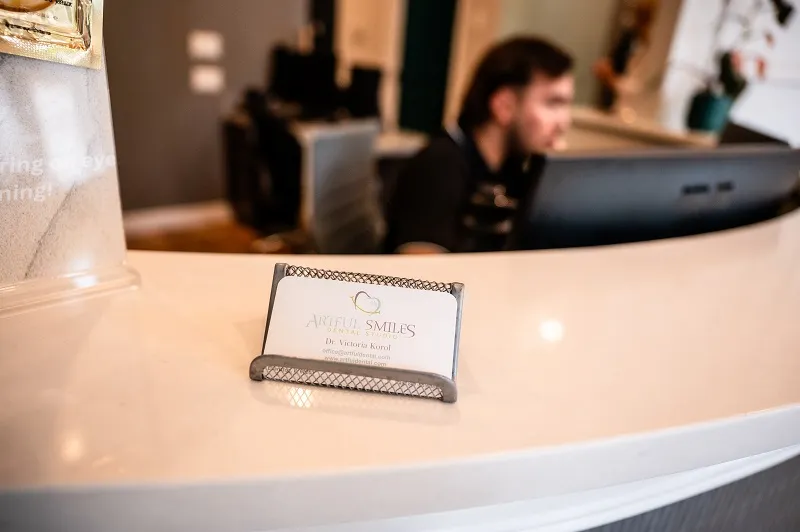 Close-up of a smooth, beige reception counter with a small business card holder and a staff member visible in the background