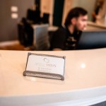 Close-up of a smooth, beige reception counter with a small business card holder and a staff member visible in the background